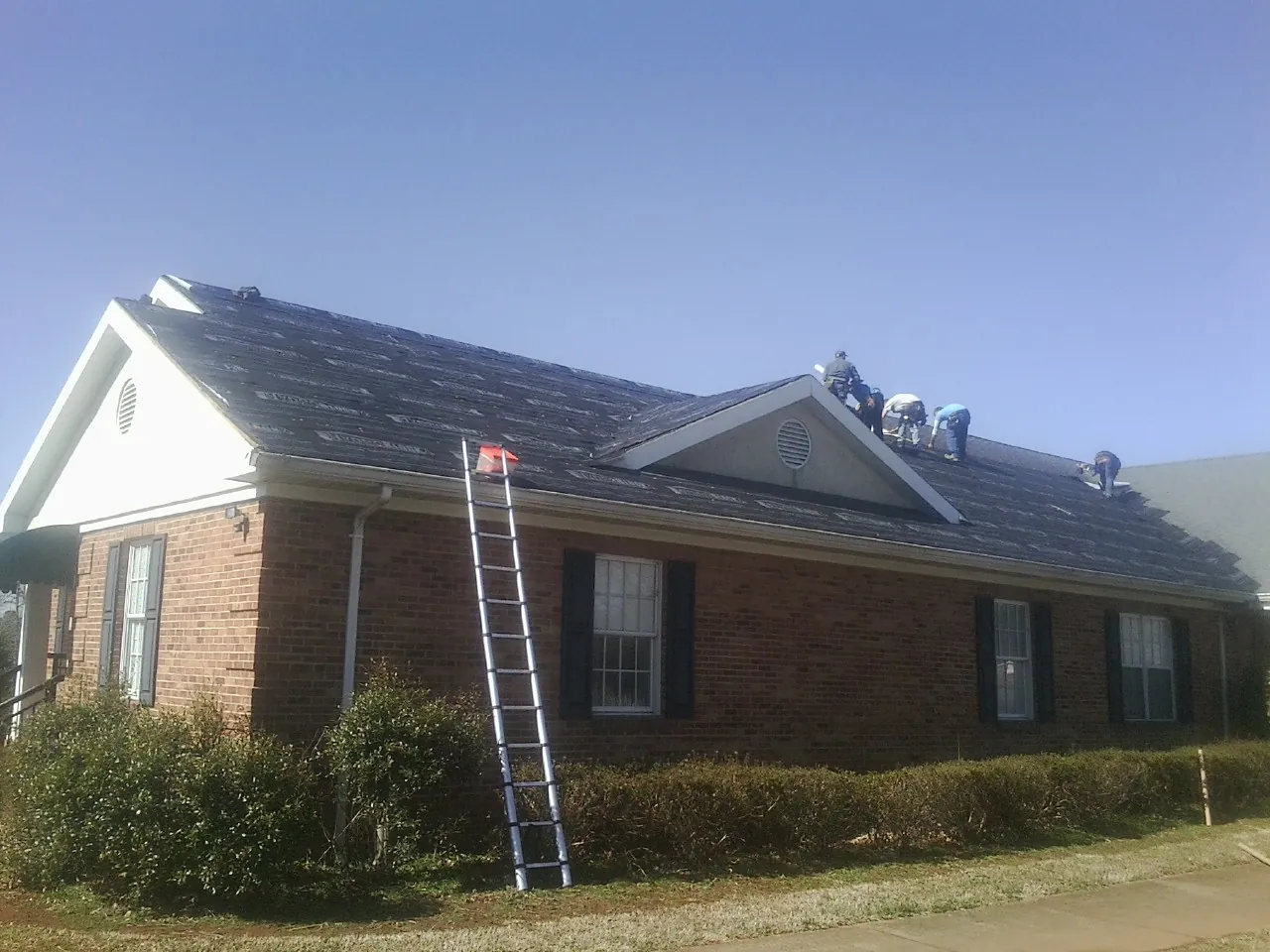 Crew tearing shingles off a brick ranch roof with a ladder set — Emergency Roof Repair work by our crew in Monticello